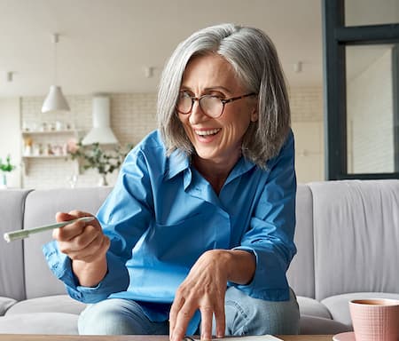 An elder lady smiling and pointing at a computer screen